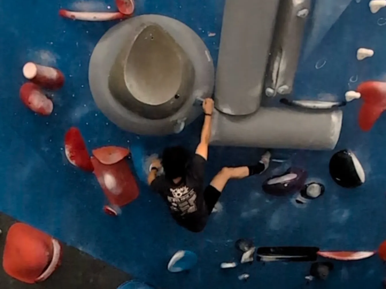 Me on a blue bouldering wall, holding the edge of a big grey volume with my feet up on the wall.